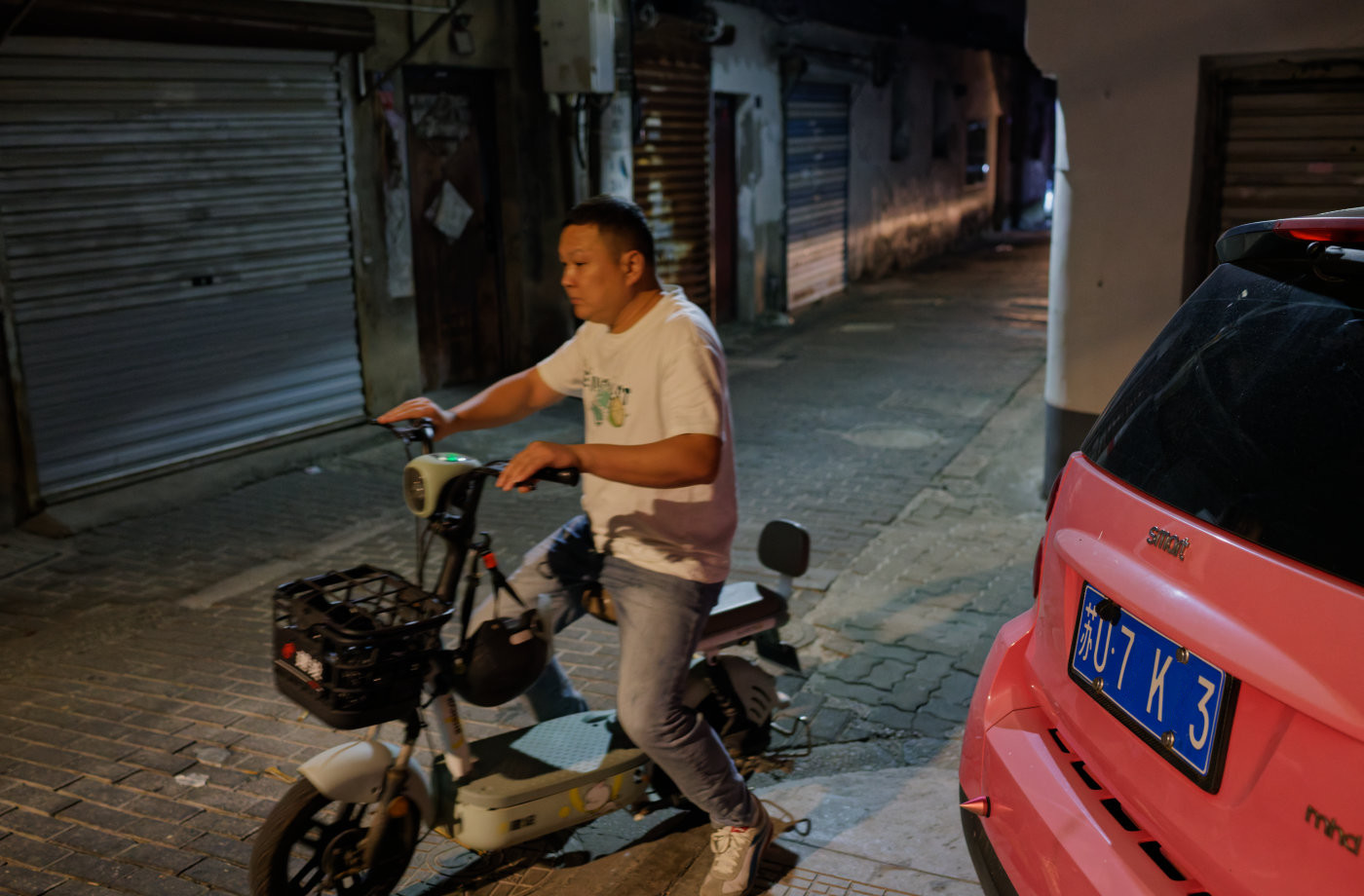 街角路口，一辆停在路边的粉红色汽车格外醒目，正好有人骑着电动车经过。
