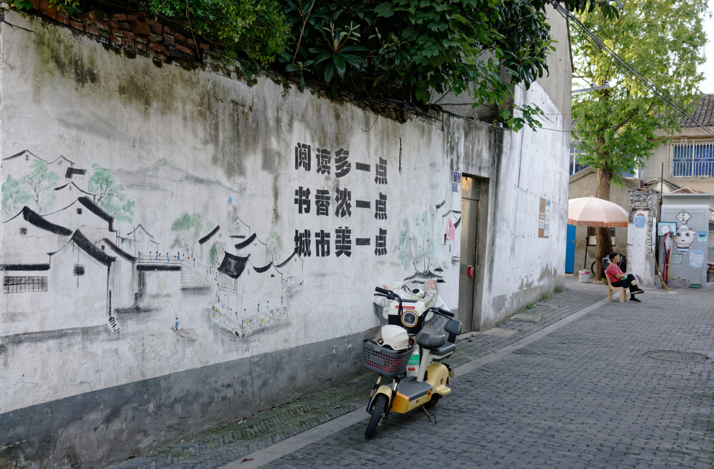 墙上的街巷图与“书香城”标语，在电动车旁慢慢褪色。