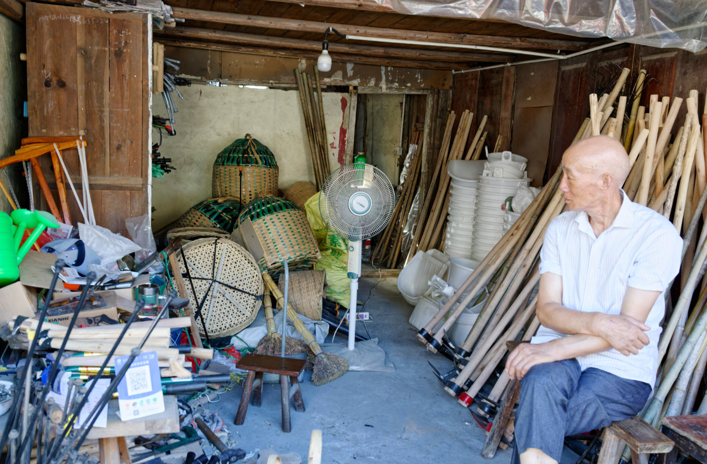 竹编物件与农具堆在屋里,老人坐在一旁悠然自得。