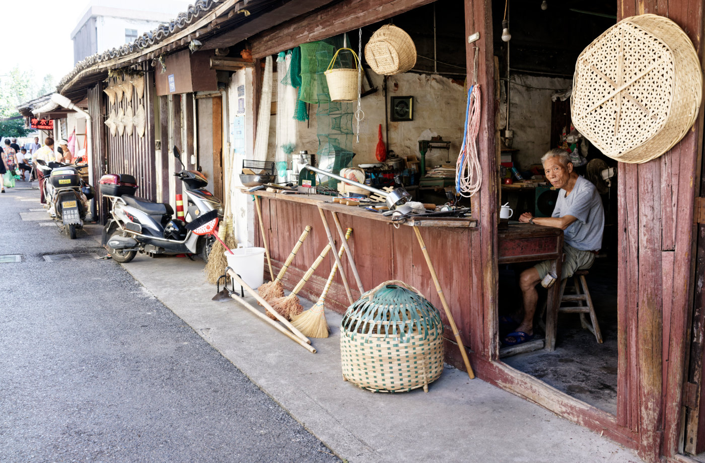 老店门口挂着竹篮、筛子和扫帚,老人坐在铺子里望向街面,像在守着一段旧时光。