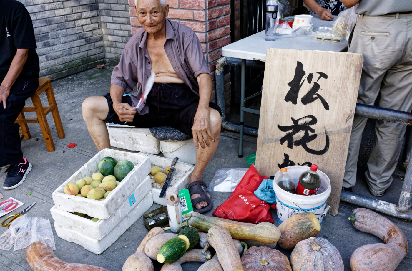 街边摊位上摆着南瓜、桃子和西瓜,还有牌子上写着松花糕,老人拿着扇子坐在一旁,像这段短短散步的收尾。