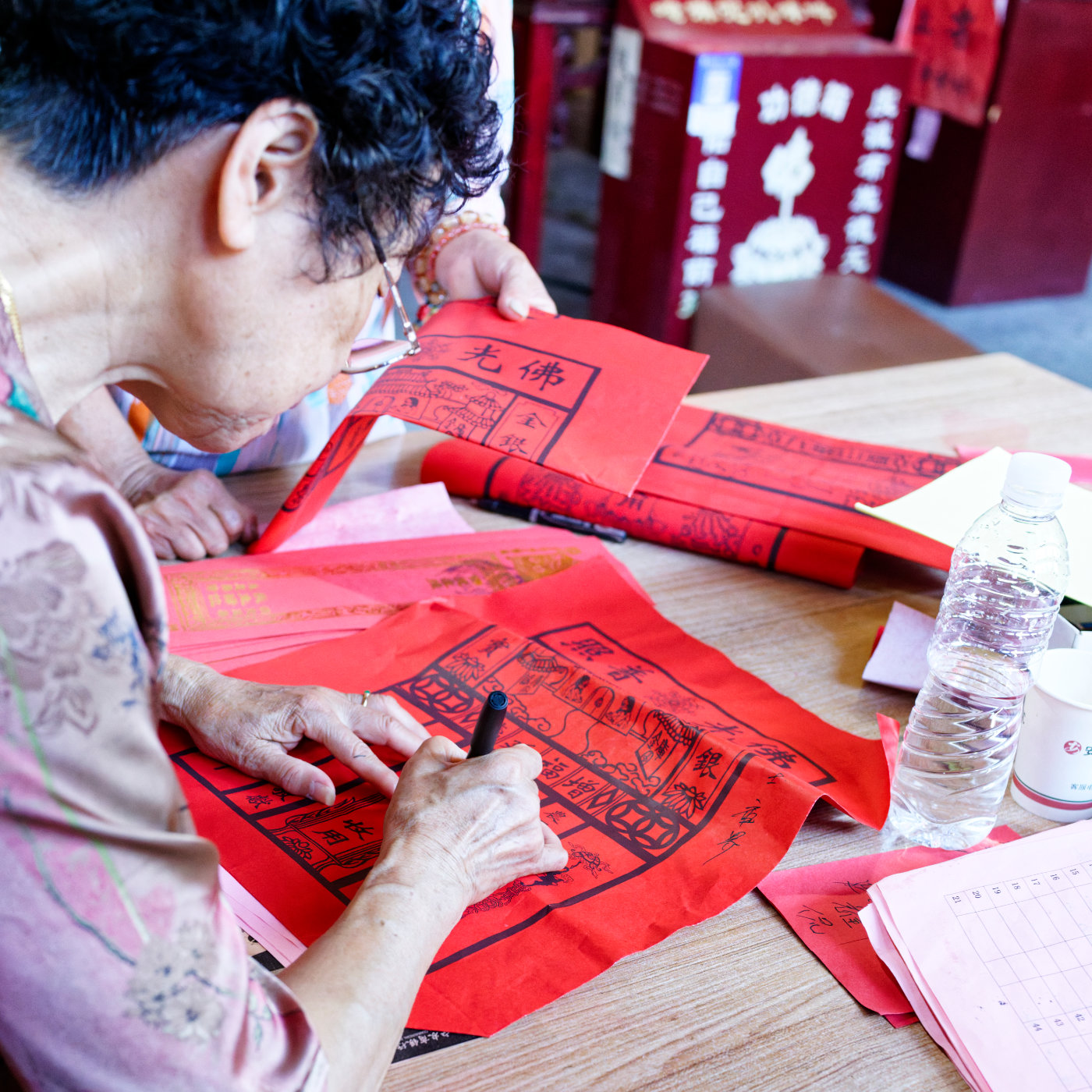 一位香客正在书写纸钱上的文字,仪式也因此变成了一件需要亲手完成的事情。